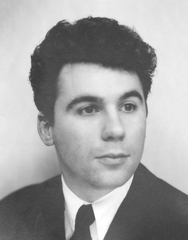 Claude Nougaro posing emotionless with head slightly turned left and looking forward, wearing dark blazer, white shirt, and black tie, 1955