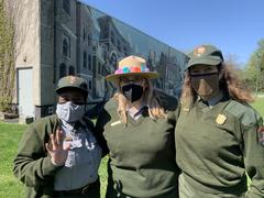 Three female park rangers posing in front of a mural during May Pole Dance celebration