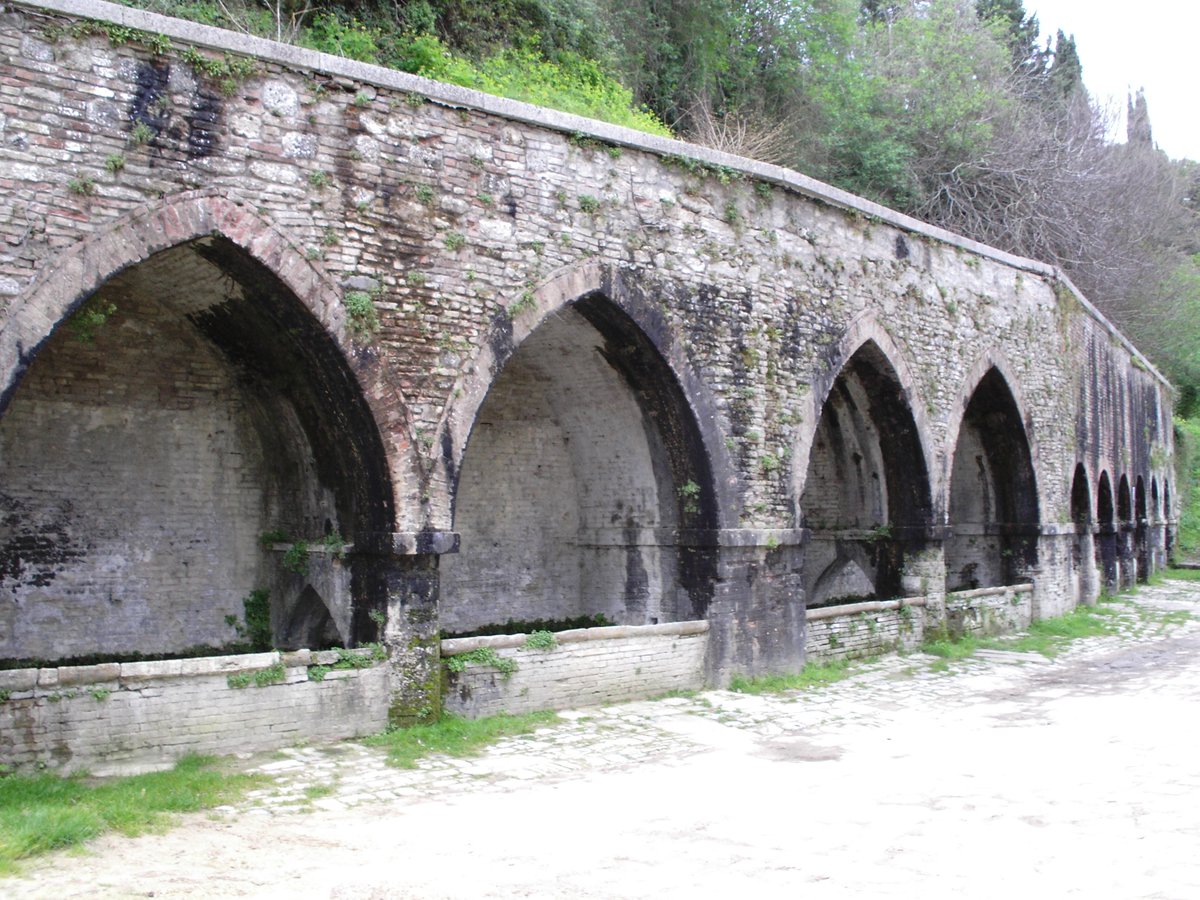 Ancient stone fountain in San Gimignano with surrounding benches and trees