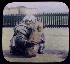 Old man squatting with arms around a sheep skin water container at Gulistan station on the Quetta Railway