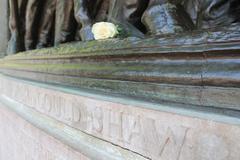 Close-up of the base of Robert Gould Shaw and Massachusetts 54th Regiment Memorial showing bronze feet of soldiers and horse with a white rose placed among them, light pink stone engraved with Robert Gould Shaw