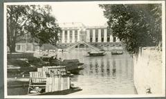 Grand waterside palace with columned portico and double steps by the water, boats moored on bank and water