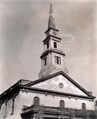 Looking up at second floor and steeple of St. Mark's Church with skywriting spiral to the left of the steeple and pastoral scene painted in the pediment