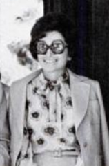 Smiling white woman with bouffant dark hair, light-colored suit, and large sunglasses