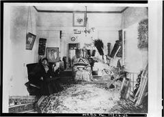 Queen Liliuokalani in her bedroom at Washington Place surrounded by kāhili and portraits of her husband John Owen Dominis and brother Kalakaua