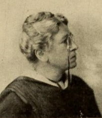 Profile portrait of an older white woman with white hair in an updo, wearing pince-nez glasses on a lanyard and a dark academic robe