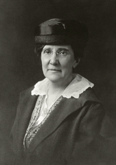 Formal half-length portrait of Dr. Caroline E. Spencer wearing eyeglasses, hat, coat, and lace-collared dress