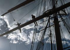Two park rangers standing on a foot rope aloft holding a spar on sailing ship deck