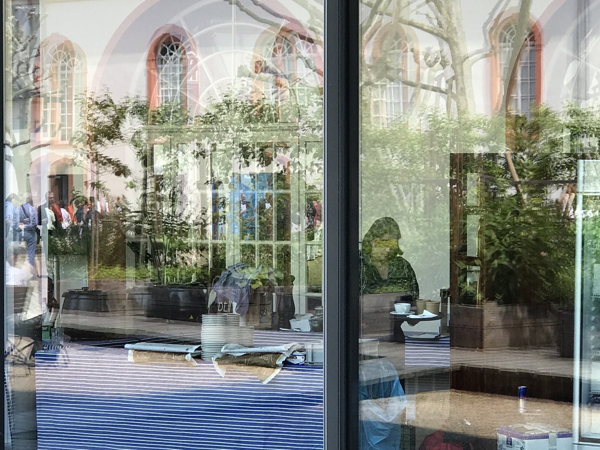 View through a window of the inner courtyard at the Mainz State Museum showing the café inside and reflections of the courtyard with trees and opposite wall creating overlapping, confusing visuals