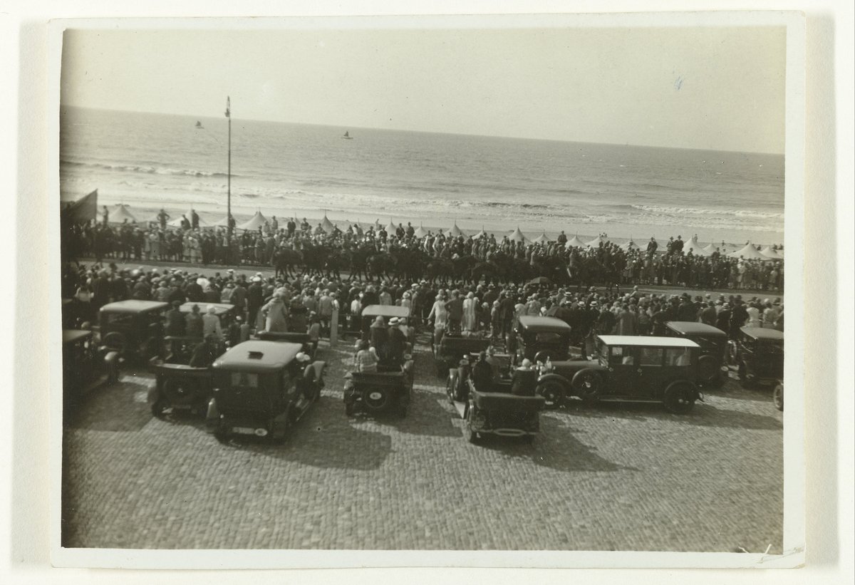 Vintage photograph of cars and people on the boulevard of Scheveningen watching a parade of horse riders with the sea in the background