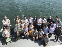 Group of volunteers and NPS staff smiling on the stern of a boat with water ripples behind