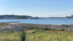 A panoramic view from Slate Island in Massachusetts showing the Atlantic Ocean with rocky coastline and lush green vegetation under a clear blue sky