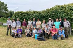 Group photo of volunteers and NPS staff smiling under grape vines on Grape Island
