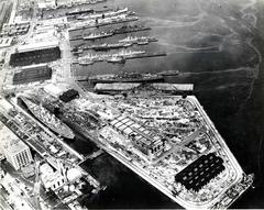 Aerial view of U.S. Navy Boston Naval Shipyard in July 1943 featuring USS Iowa battleship in dry dock, USS Bunker Hill aircraft carrier, and Baltimore-class heavy cruiser