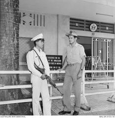RAAF Sergeant Robert Alexander McWhinney talking with a South Vietnamese policeman outside the U.S. Embassy in Saigon with barbed wire defenses