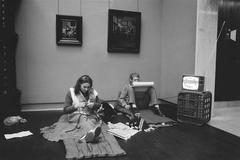 Person knitting and watching TV in front of old master paintings during Rijks and Stedelijk Museum occupation in Amsterdam