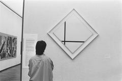 Black and white photograph of Piet Mondriaan's artwork 'Compositie van 2 lijnen' exhibited in Stedelijk Museum Amsterdam with notice of threatened sale