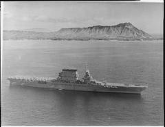 Aerial view of the USS Lexington aircraft carrier with aircraft on deck and Diamond Head in the background