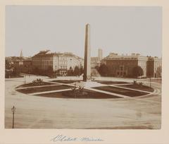 Obelisk monument at Karolinenplatz roundabout in Munich Germany surrounded by circular grassy area and pedestrian paths