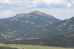 Twin Sisters Peaks viewed from Many Parks Curve Overlook in Rocky Mountain National Park with lush green forest and blue sky